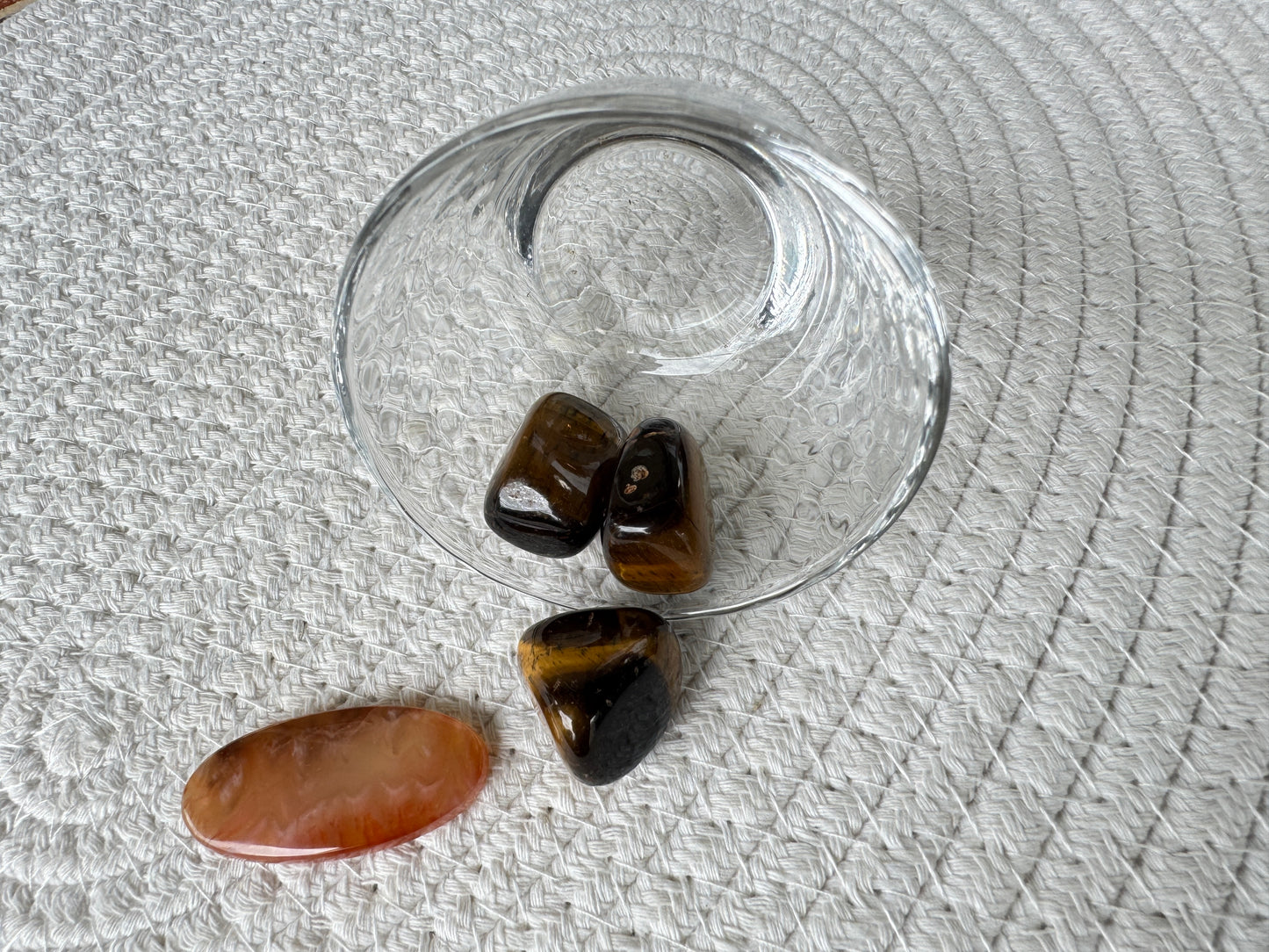 白い布地の上に配置された4つの天然石。中央には横向きのカーネリアン(カボション)、その周囲に3つのタイガーアイ(タンブル)がゆるやかに配置されている。