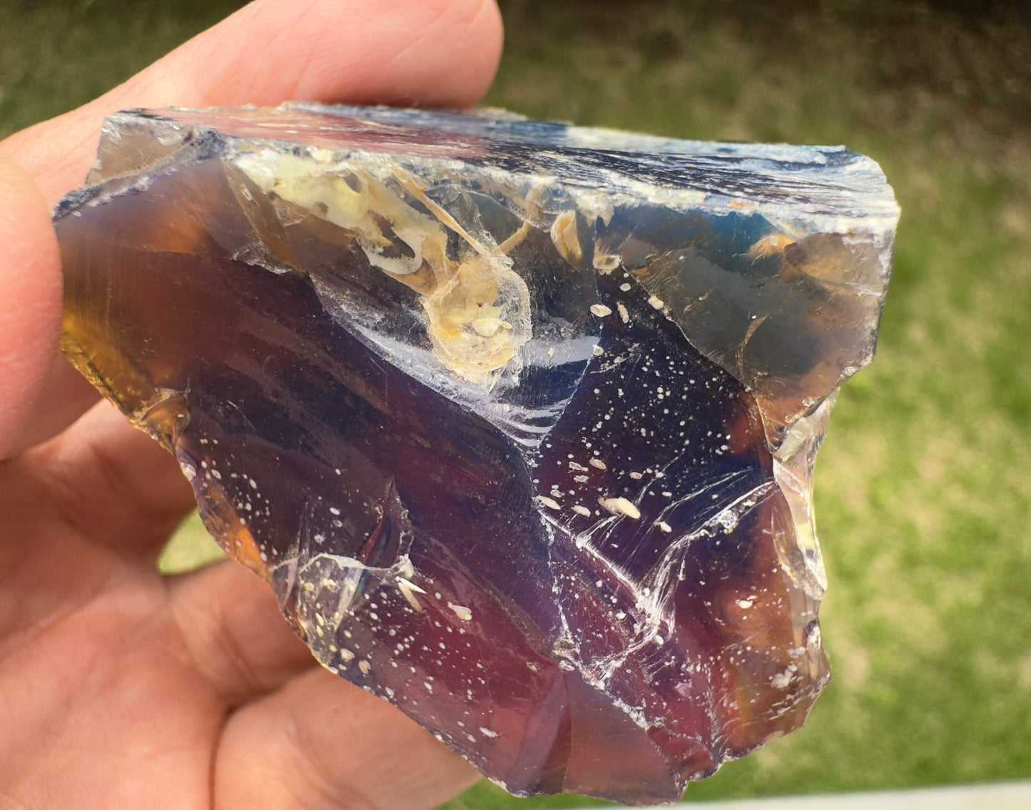 平らな面に光が反射し、内部の気泡や白い斑点が幻想的に広がっている。紫〜琥珀色のグラデーションが印象的。